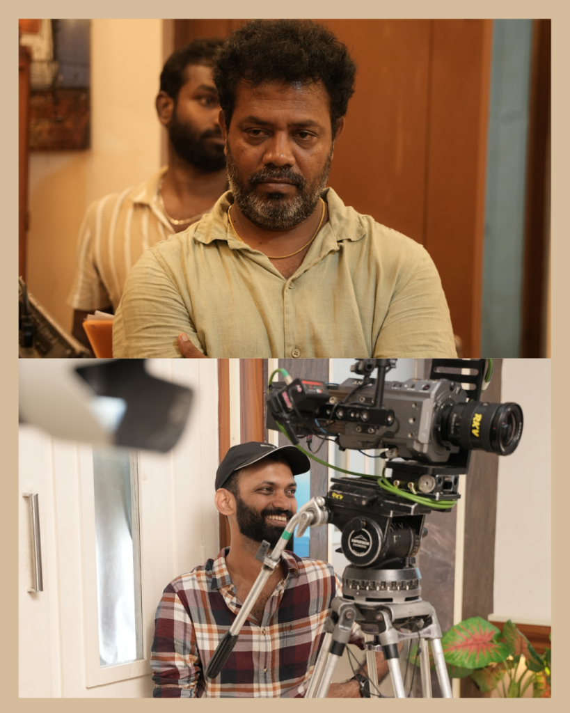 Two men on a film set: a serious bearded man in a beige shirt stands in the foreground while a smiling cameraman operates a professional camera on a tripod in the background.